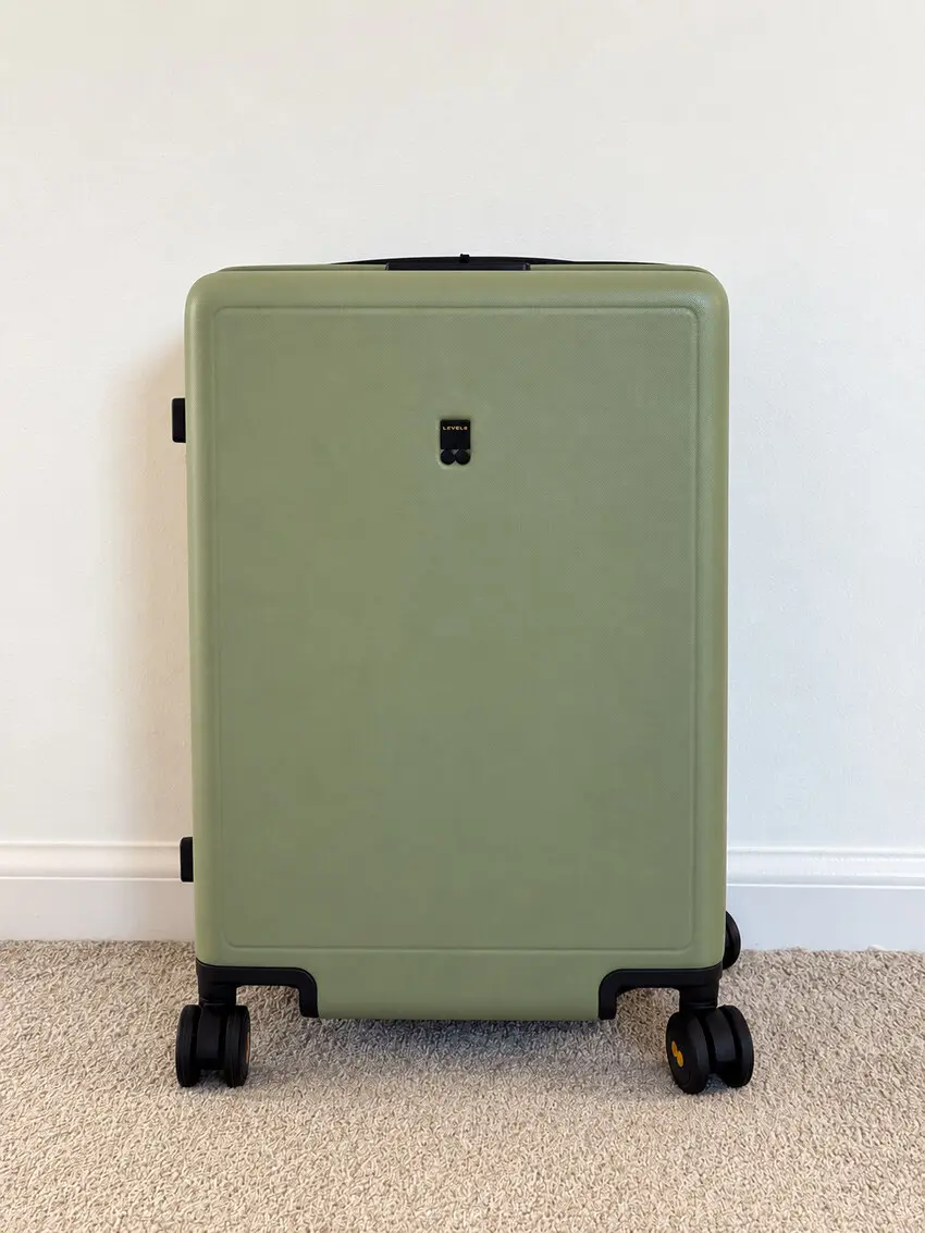Green LEVEL8 hard shell carry-on suitcase with four spinner wheels standing against a white wall