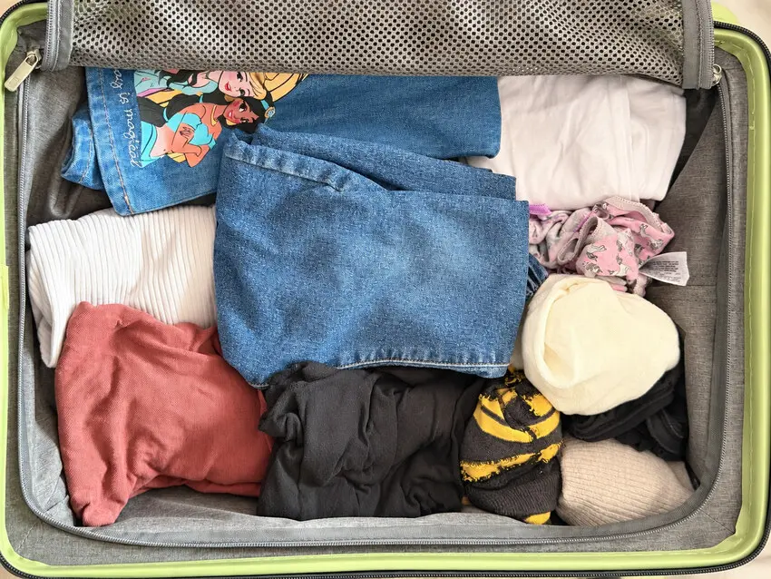 Rolled clothes for a family overnight stay packed in a green suitcase, with the mesh divider pocket open at the top