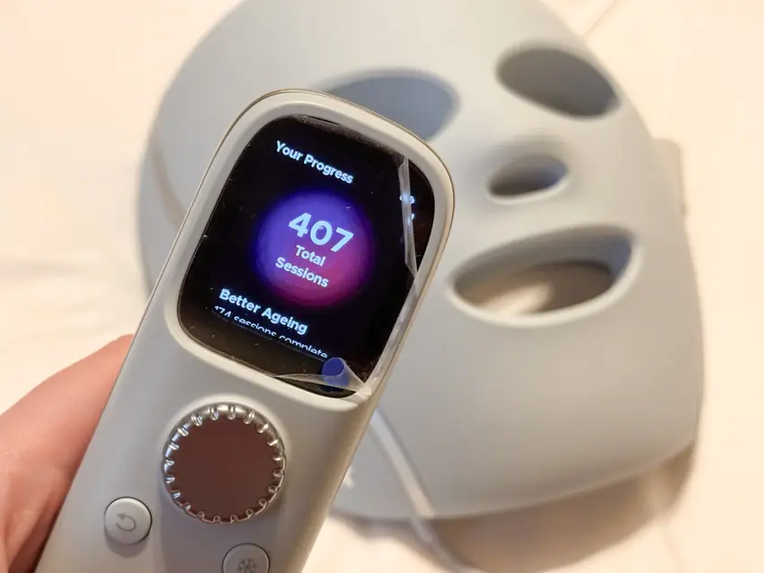 Shark CryoGlow controller showing 407 total sessions, held in front of the grey LED face mask.