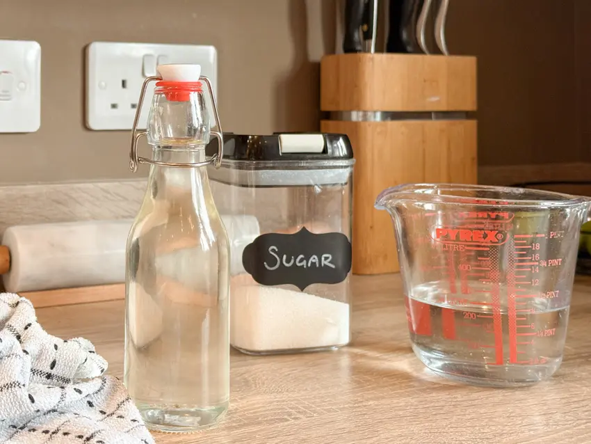 Homemade simple syrup in a swing-top glass bottle beside a sugar container and measuring jug