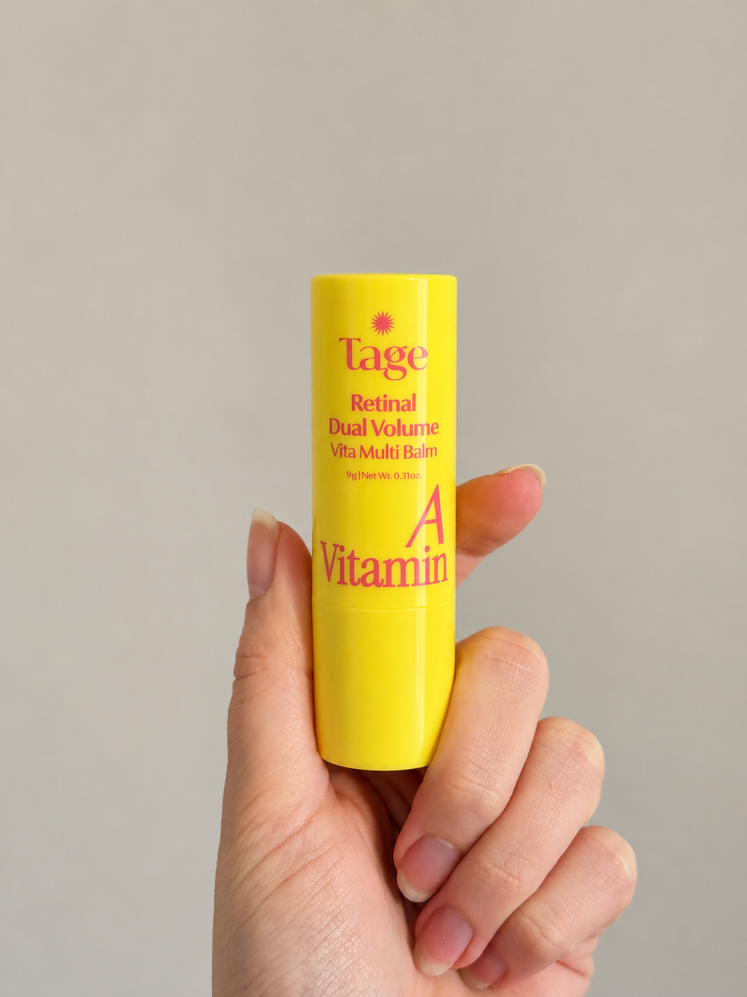 Hand holding the Tage Vita A Retinal Dual Volume Multi Balm stick against a neutral background