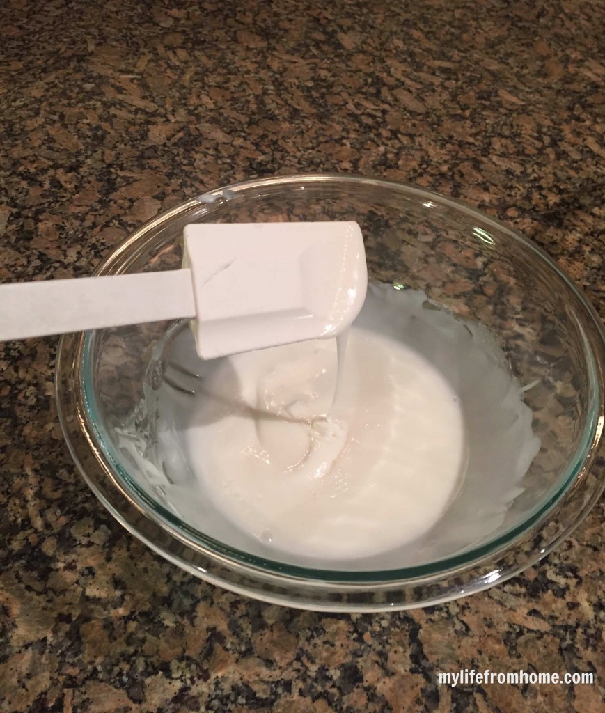 Vanilla glaze in a glass bowl with a spatula ready to drizzle over cookies
