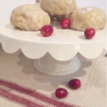 Glazed vanilla scone cookies on a white scalloped cake stand with fresh cranberries scattered around