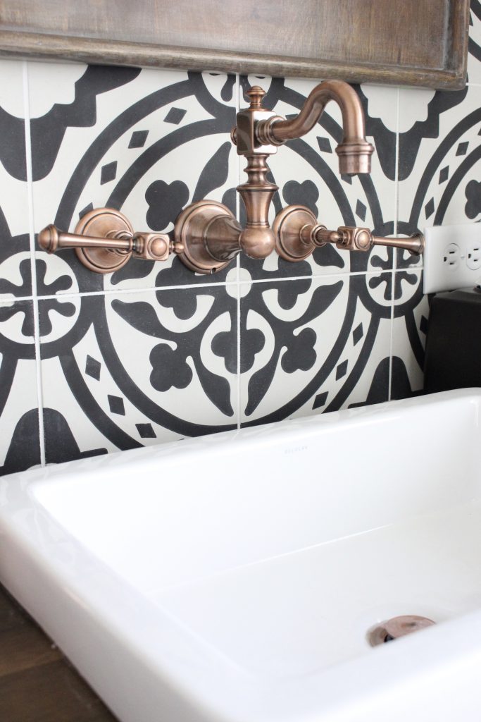 Close up of wall mounted copper faucet against black and white patterned cement tile in a modern farmhouse bathroom