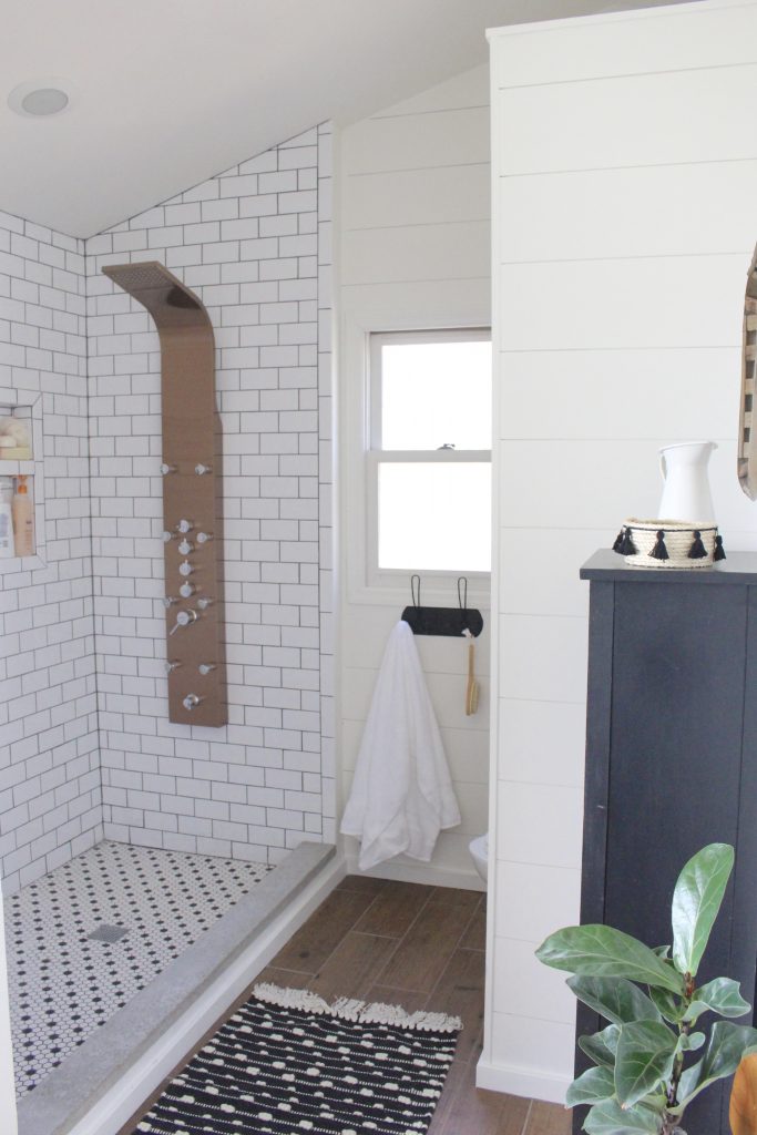 Walk in shower with white subway tile walls, copper shower panel tower, and black and white penny tile floor in a modern farmhouse bathroom