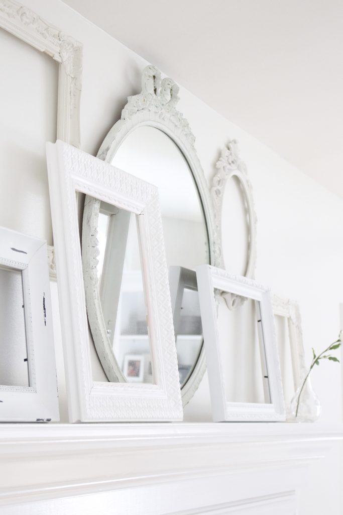 A shabby chic white mantel- layered frames- white mirror- all white decor- romantic design- fireplace decor- mantel decor- home design- decor ideas- mantles- french country style mantel- DIY- Do it Yourself- DIY projects- room design- wall decorating ideas- gallery wall- room decor ideas- decoration ideas- farmhouse style chandelier- romantic style