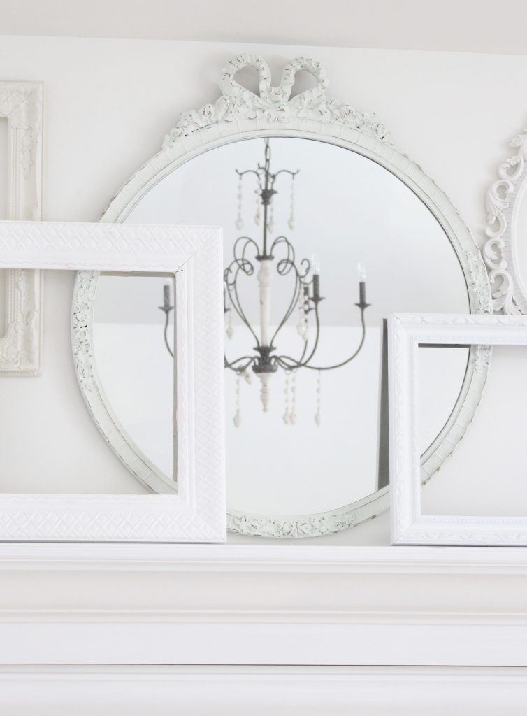 A shabby chic white mantel- layered frames- white mirror- all white decor- romantic design- fireplace decor- mantel decor- home design- decor ideas- mantles- french country style mantel- DIY- Do it Yourself- DIY projects- room design- wall decorating ideas- gallery wall- room decor ideas- decoration ideas- farmhouse style chandelier