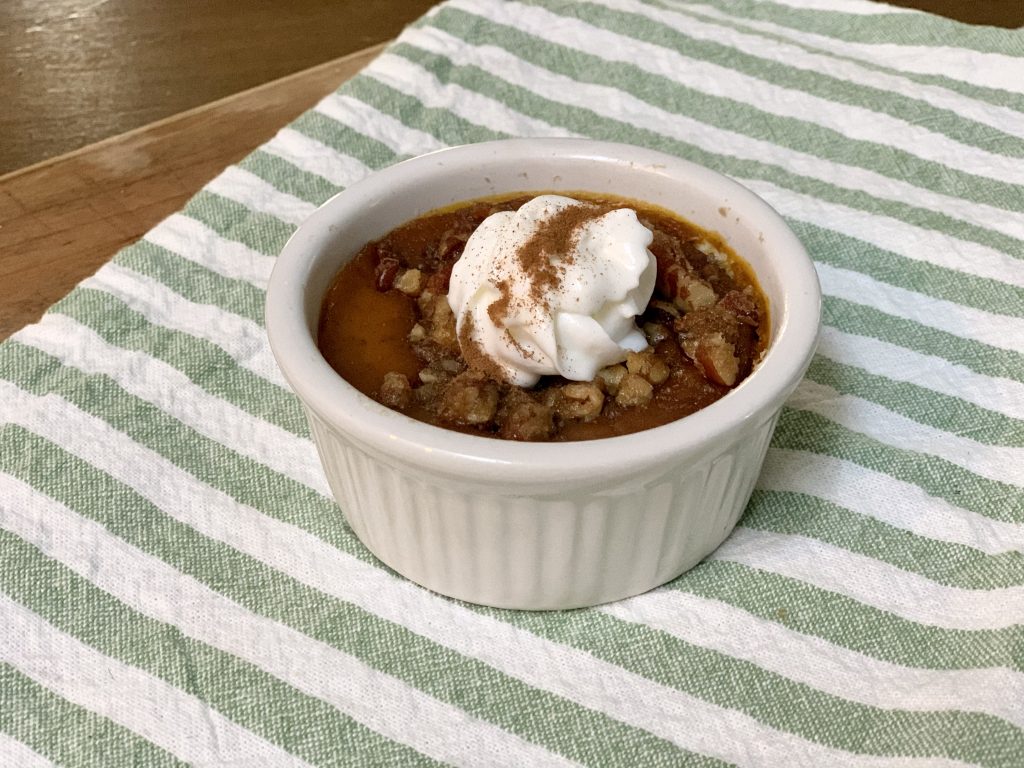 Baked pumpkin custard in a white ramekin topped with crunchy pecans and a dollop of whipped cream