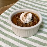 Baked pumpkin custard in a white ramekin topped with crunchy pecans and a dollop of whipped cream