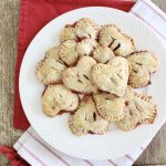 A plate of baked heart shaped hand pies with fork crimped edges and sparkling sugar seen from above on a red napkin