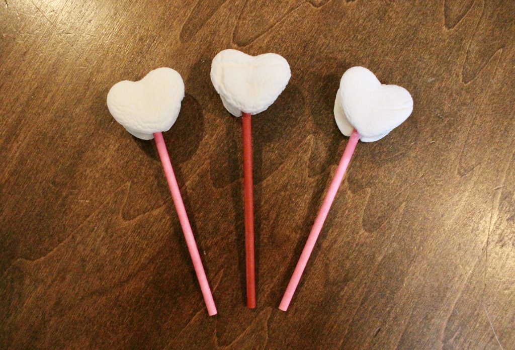 Three heart shaped marshmallows on pink and red lollipop sticks before being dipped in chocolate