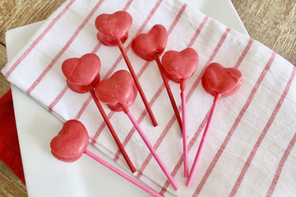 Heart shaped marshmallow pops coated in pink chocolate on a red and white striped tea towel