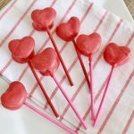 Heart shaped marshmallow pops coated in pink chocolate on a red and white striped tea towel
