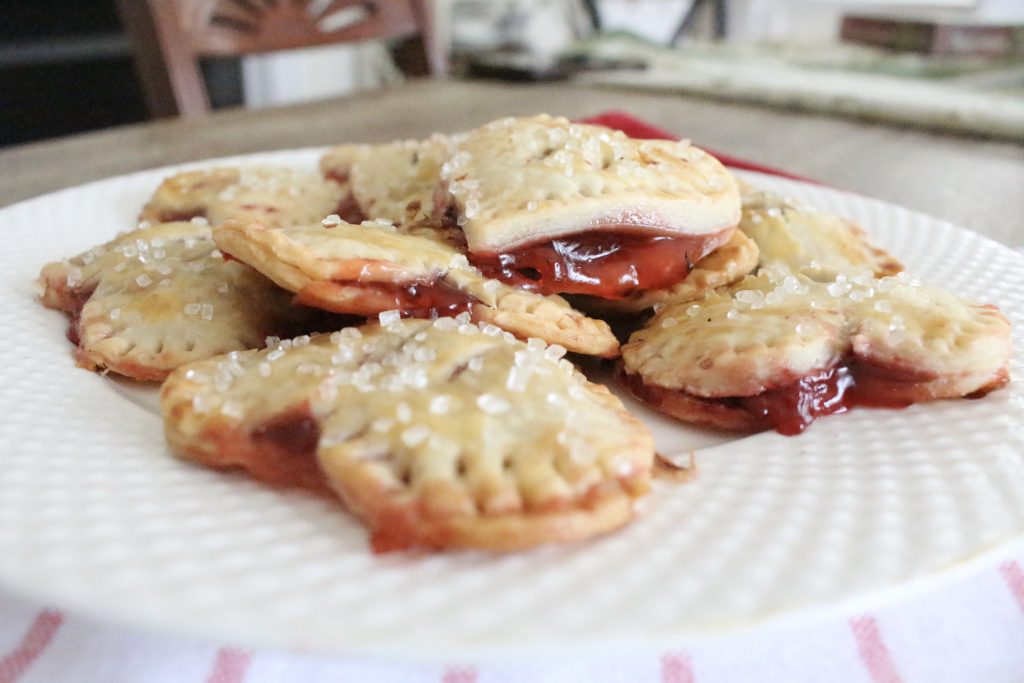 Golden heart shaped hand pies with sugar crystals on top and strawberry filling visible at the edges on a white plate