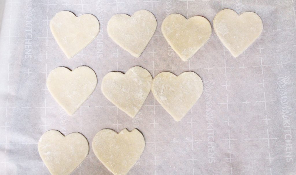 Nine heart shaped pastry cutouts arranged on parchment paper ready to be filled