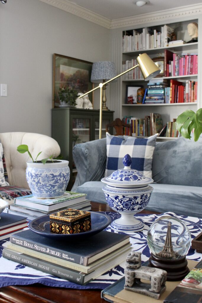 Styled coffee table with stacked books, blue and white ginger jar, Paris snow globe, and brass cantilever lamp