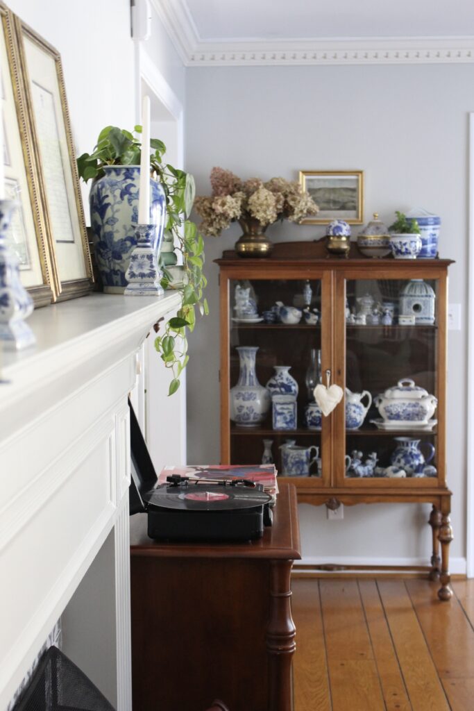 Vintage record player on wooden cabinet beside a glass-front china cabinet filled with blue and white ceramics