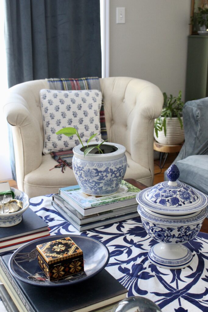 Cream tufted armchair with block print cushion beside a styled coffee table with blue and white chinoiserie