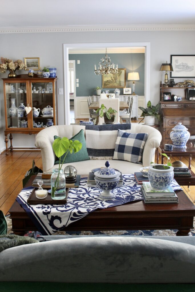 Curved cream sofa with cushions in the centre of a colourful home library with china cabinet and view into dining room