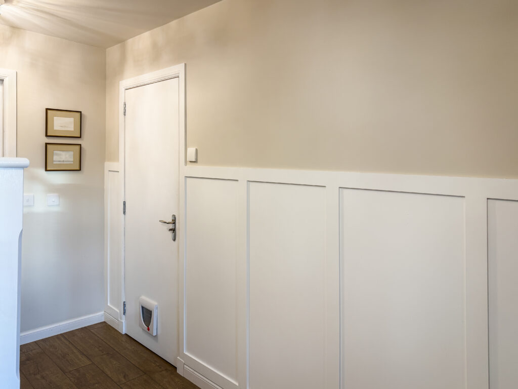 Finished hallway with white wall panelling, Valspar Goose Feathers walls, wooden flooring and garage door with cat flap