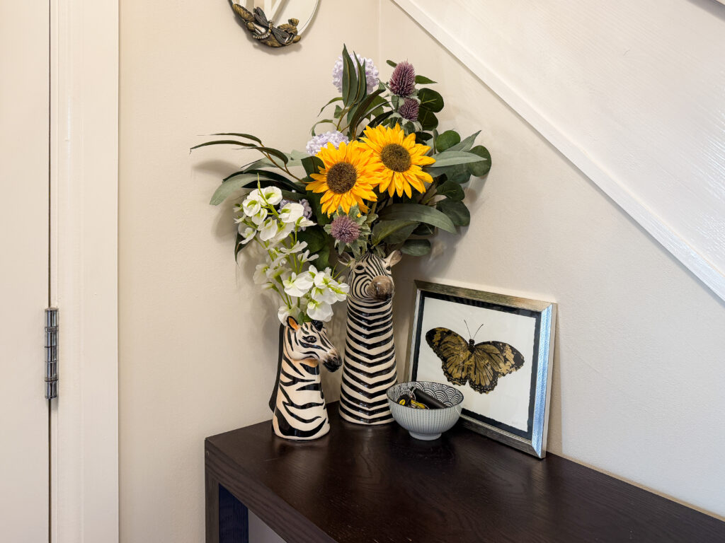 Styled hallway console table with zebra vases, sunflowers and framed butterfly print tucked under the staircase