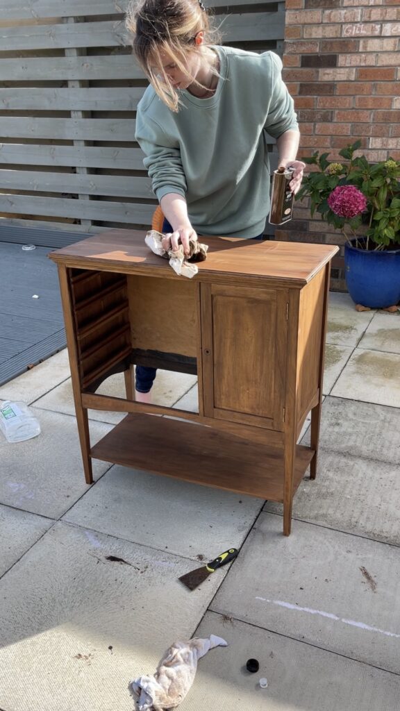 Applying wood dye to a restored vintage music cabinet with a lint-free cloth.