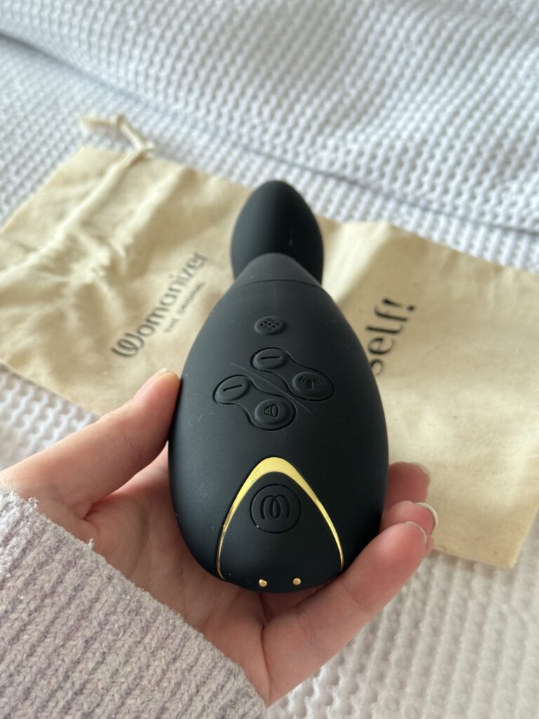 Close-up of the Womanizer Duo 2 showing control buttons and gold detailing, resting on its branded cotton storage pouch.