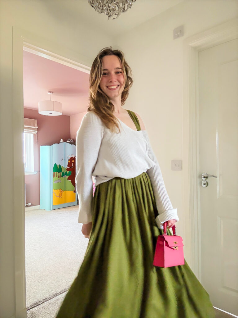Gillian wearing a floaty olive skirt with a slouchy knit and bright pink accessories, adding colour to an autumn day.
