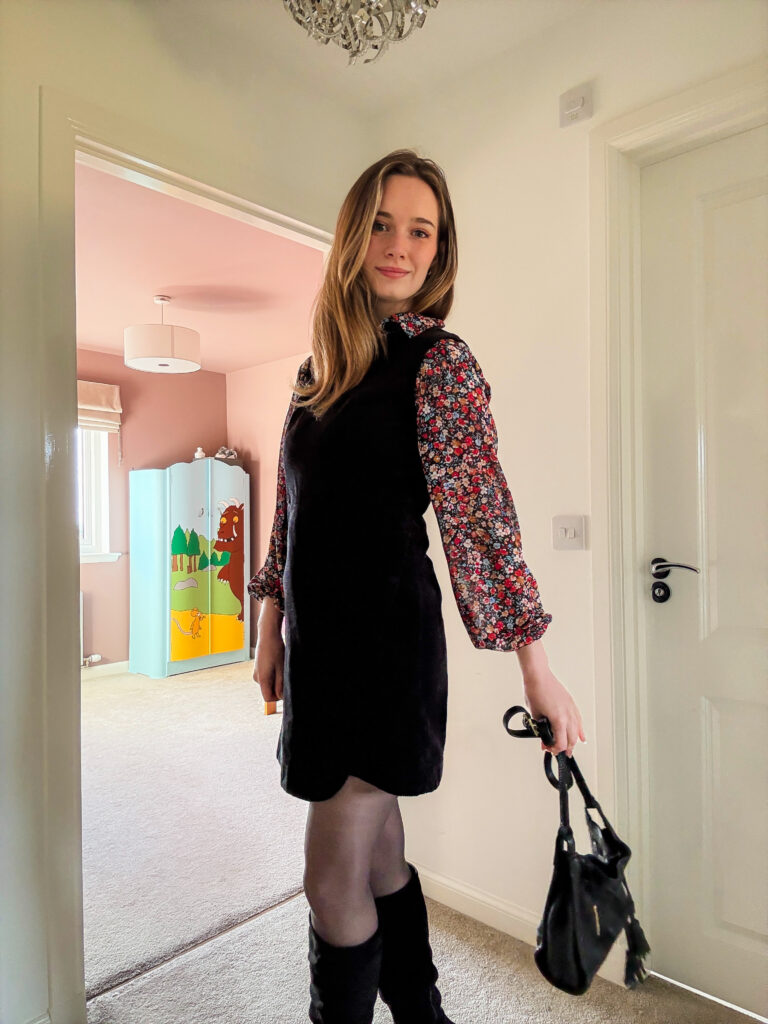 Gillian styling a scalloped black pinafore dress layered over a floral top, perfect for transitional autumn days.