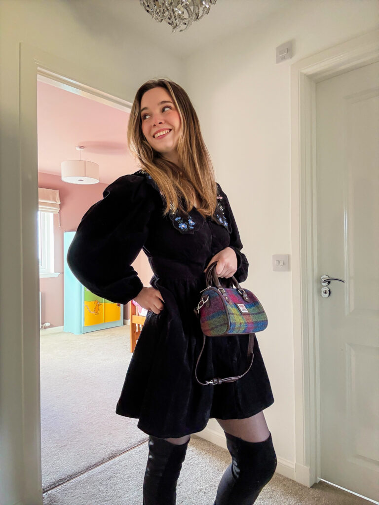 Gillian wearing a black corduroy dress with a floral embroidered Peter Pan collar, styled with tights and boots for autumn.