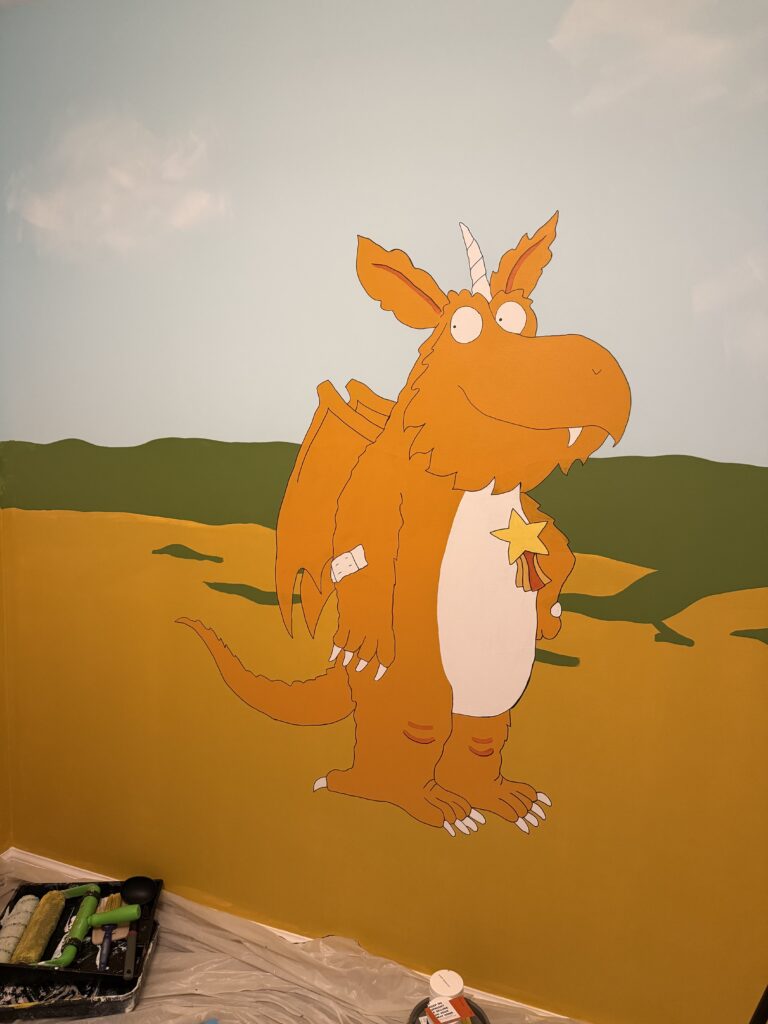 Hand-painted mural of Zog the dragon on a yellow and green landscape in a children's bedroom, partially completed.