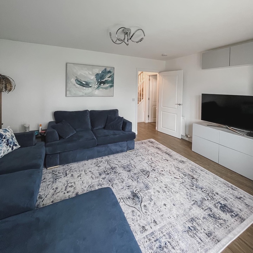 Before image of living room with navy velvet sofas, patterned rug, white walls, and wall art above the sofa.