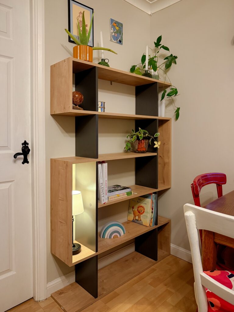 Geometric oak and grey display bookshelf styled with plants, cookbooks and children's books in a dining room