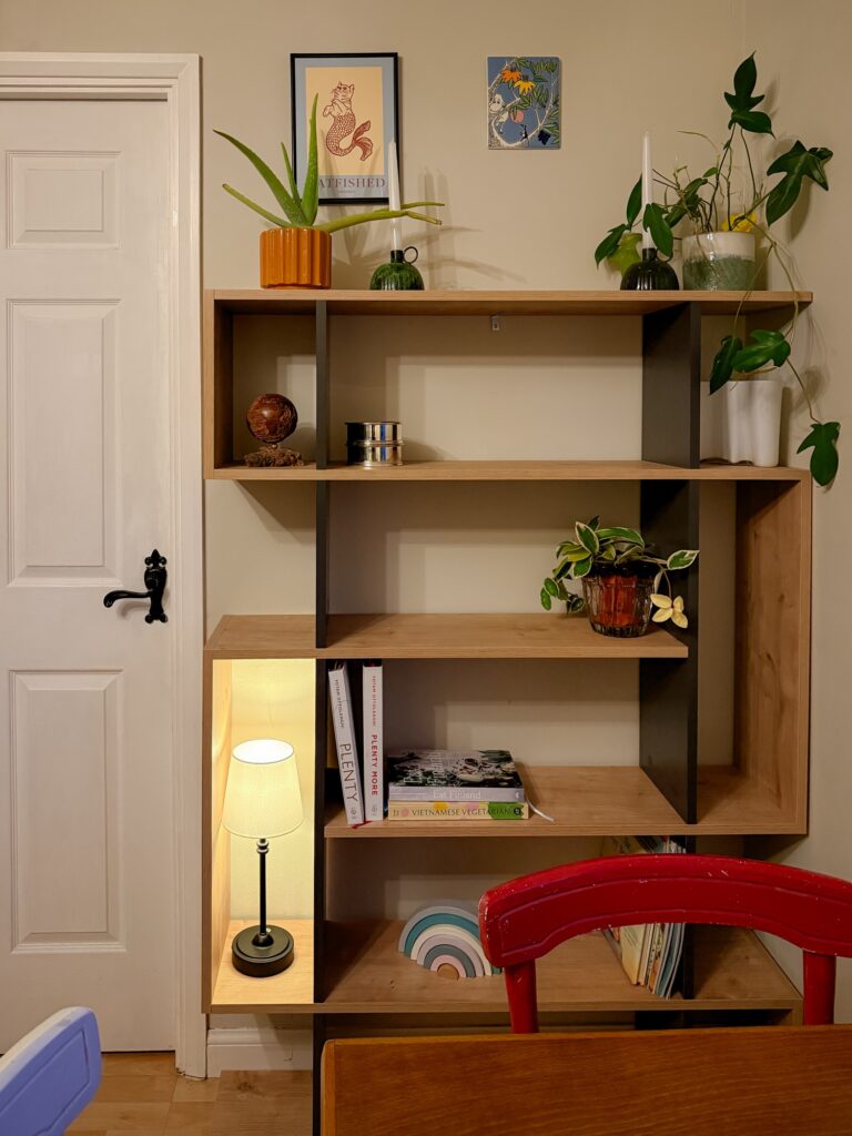 Oak and grey geometric bookshelf styled with trailing plants, cookbooks, and decorative objects in a dining space