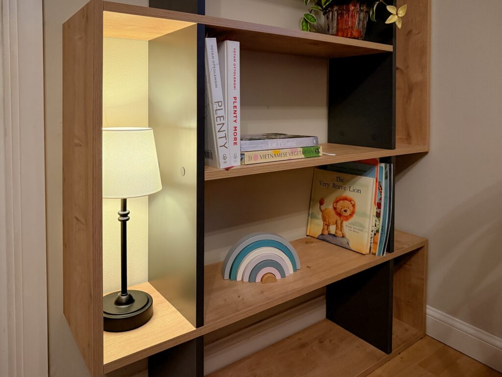 Close up of bookshelf lower shelf with children's books, a wooden rainbow stacker, and a cosy lamp