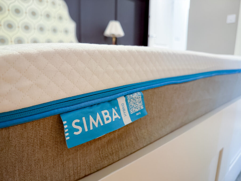 Close-up of Simba Original Hybrid mattress showing the quilted cream top layer, teal blue trim, and signature Simba Hybrid label with QR code