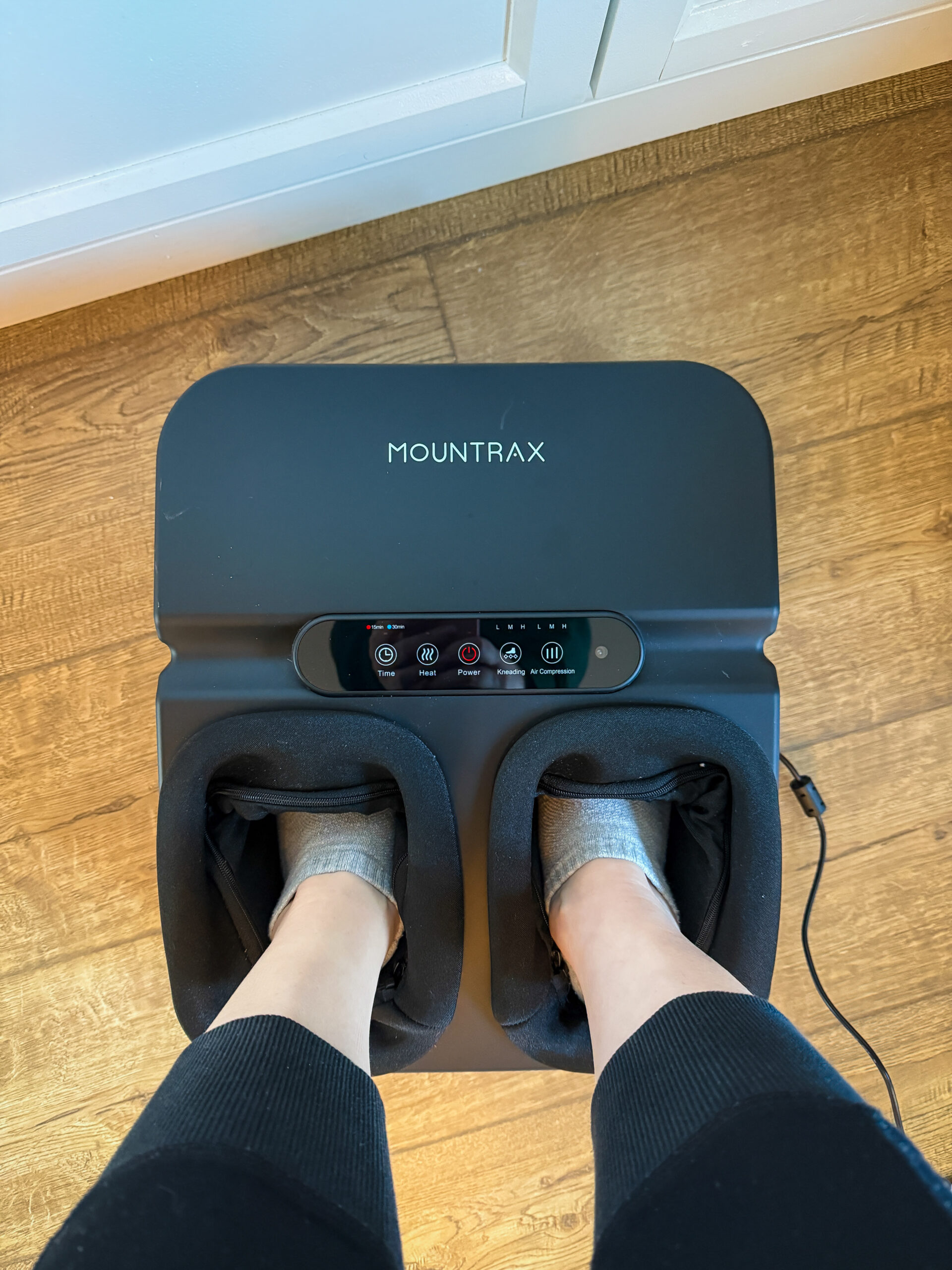 Person using MOUNTRAX electric foot massager showing touch panel controls and foot compartments