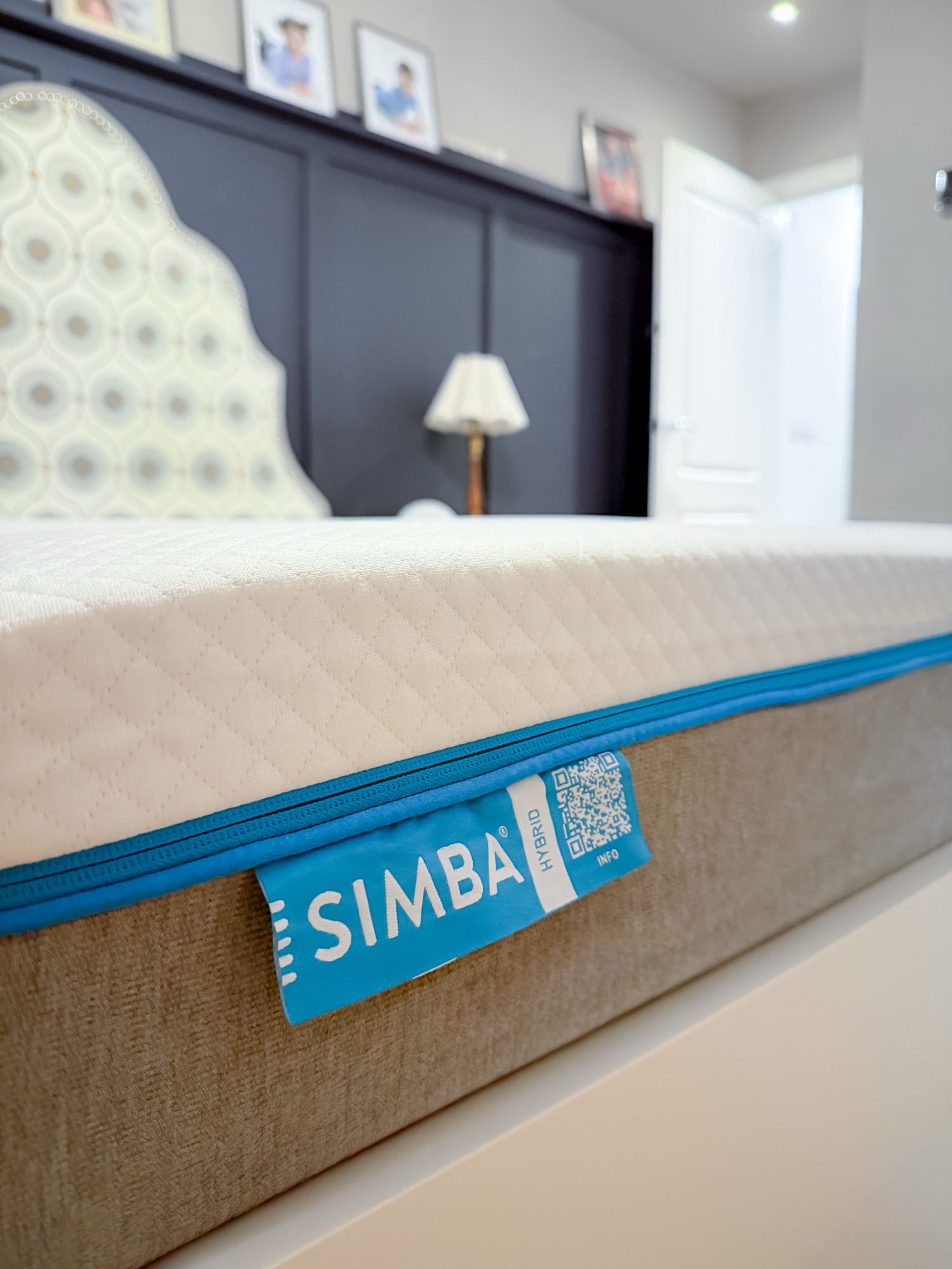 Simba Original Hybrid mattress in a styled bedroom with dark panelled headboard wall, framed photos, and classic bedside lamp