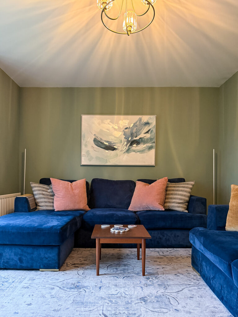 Farrow and Ball Card Room Green living room featuring brass ceiling light, navy velvet sectional with coral cushions and abstract artwork