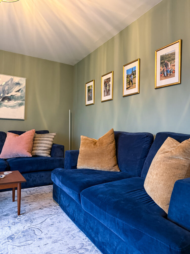 Navy velvet sofa styled with oversized mustard gold cushions and gold framed family photos in Farrow and Ball Card Room Green living room