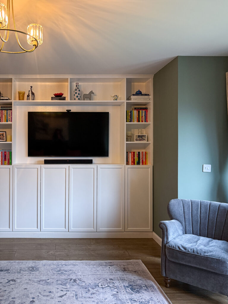 White IKEA Billy bookcase built-in wall unit with mounted TV and brass ceiling light in Farrow and Ball Card Room Green living room
