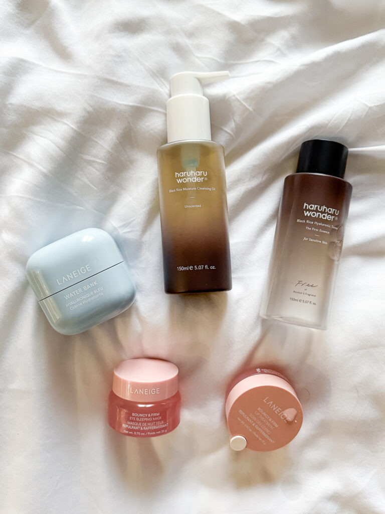 A flat lay of essential Korean skincare products for barrier health, including Haruharu Wonder Black Rice Toner and Laneige Water Bank moisturizer, arranged on white bedding.