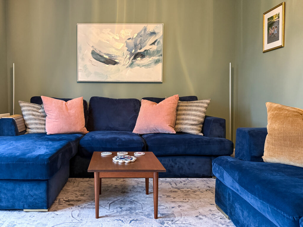 Navy velvet corner sofa with vintage mid-century coffee table and abstract canvas art in Farrow and Ball Card Room Green living room