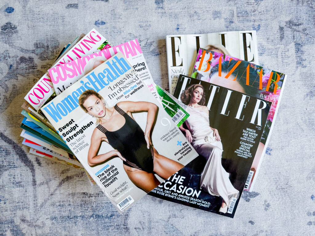 A pile of UK magazine subscriptions including Tatler, Harper's Bazaar, Elle, Women's Health, Cosmopolitan and Country Living stacked on a grey surface
