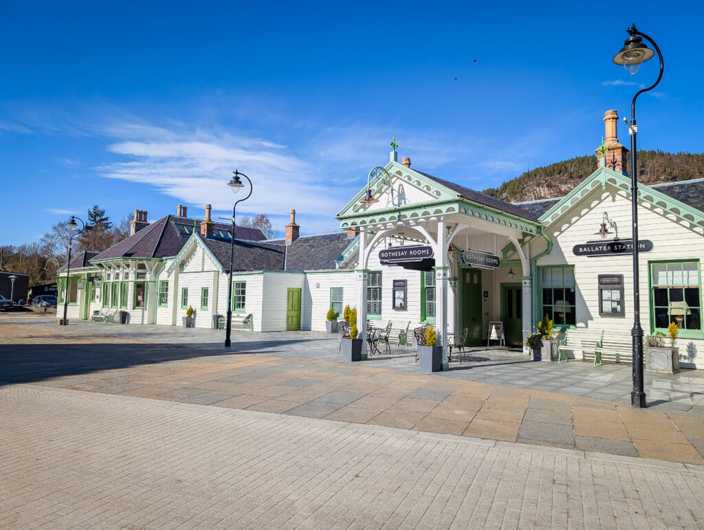 Ballater village square on a bright sunny day, showing the distinctive green and white Victorian railway station building which houses the Rothesay Rooms