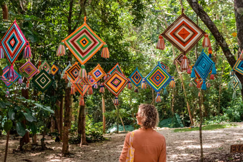 A guest admiring a canopy of colourful handwoven diamond decorations (Ojo de Dios) strung between jungle trees at Cachito de Cielo Tulum