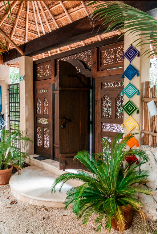 Ornate wooden entrance gate at Cachito de Cielo Tulum decorated with colourful Tibetan prayer flags and intricate carved detailing
