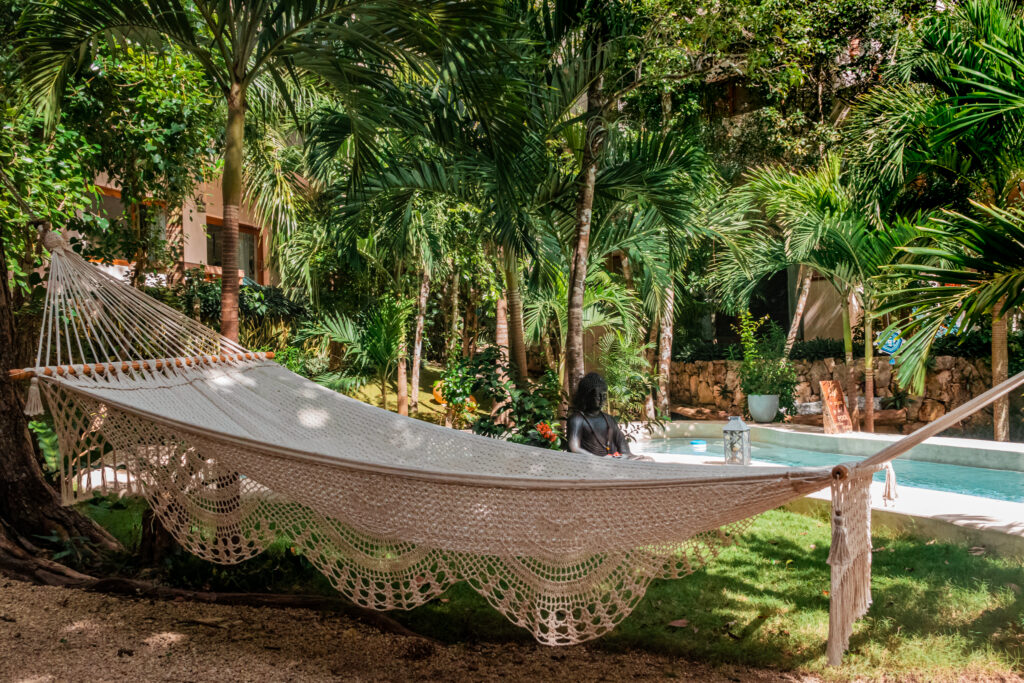 A large woven hammock in the shade of jungle palms beside the pool at Cachito de Cielo Tulum