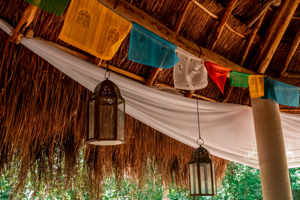 Colourful Tibetan prayer flags and hanging lanterns strung beneath the thatched roof of the communal pavilion at Cachito de Cielo Tulum