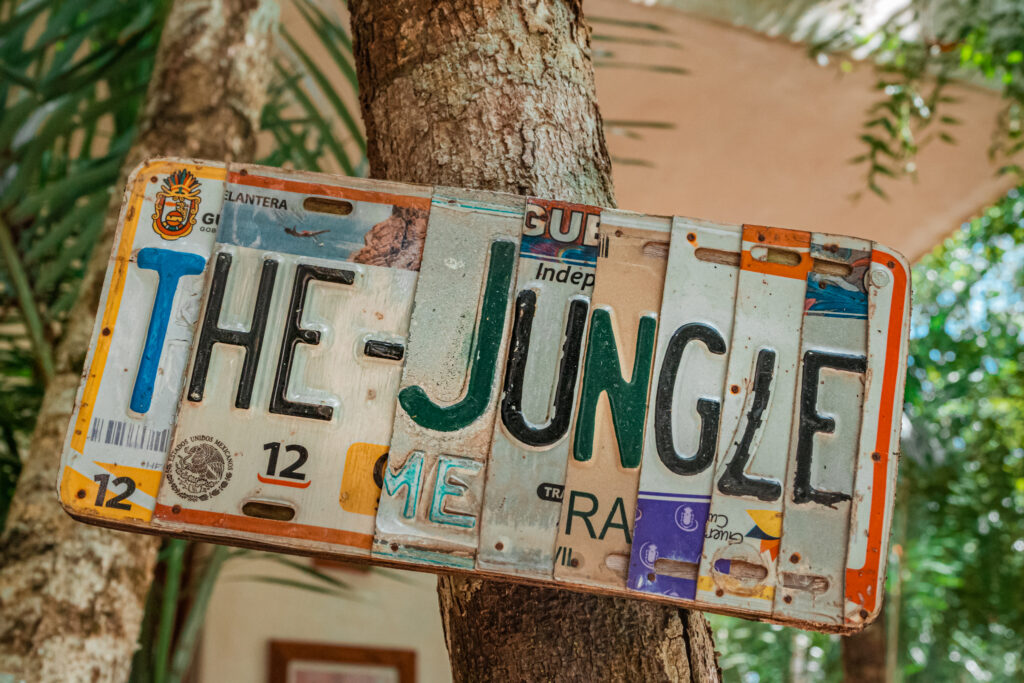 Rustic sign reading "The Jungle" made from vintage number plates nailed to a tree trunk at Cachito de Cielo Tulum